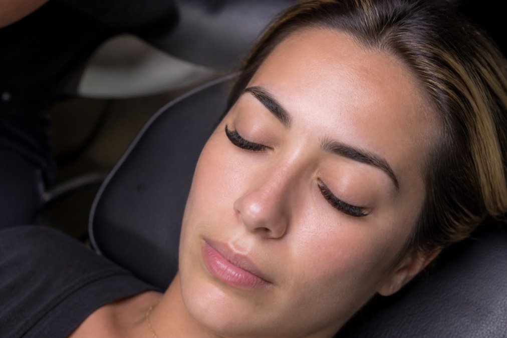 Close-up portrait of a woman with full, natural-looking lash extensions, eyes closed to show the lash line clearly, soft studio lighting