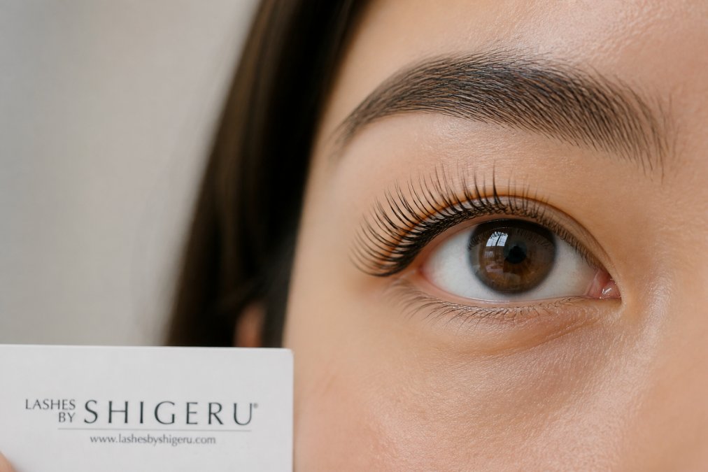Close-up of a person's eye showing full, lifted lashes with natural curl and definition against a neutral background, demonstrating the result of a professional lash lift
