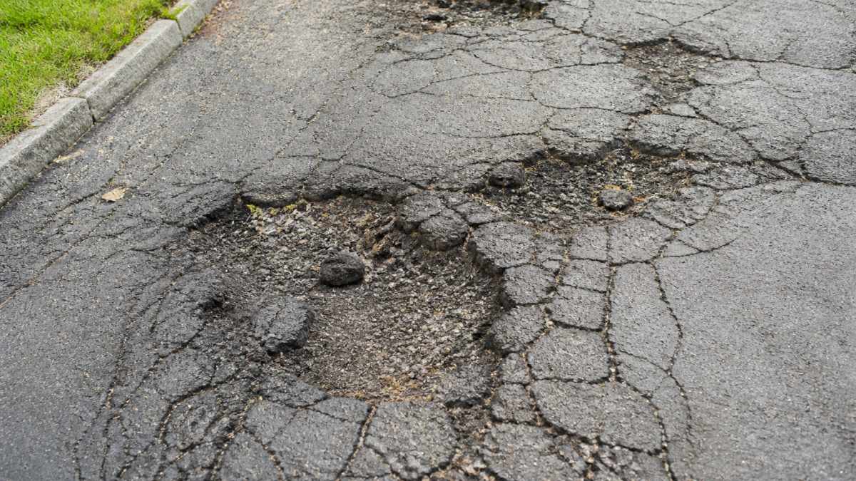 Close-up of a cracked and deteriorated driveway surface showing visible potholes, fissures and weathered asphalt in natural daylight
