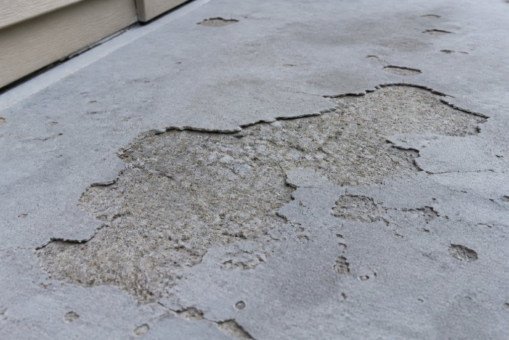 Close-up of outdoor concrete overlay showing visible spalling, delamination, and surface deterioration with weathered gray appearance