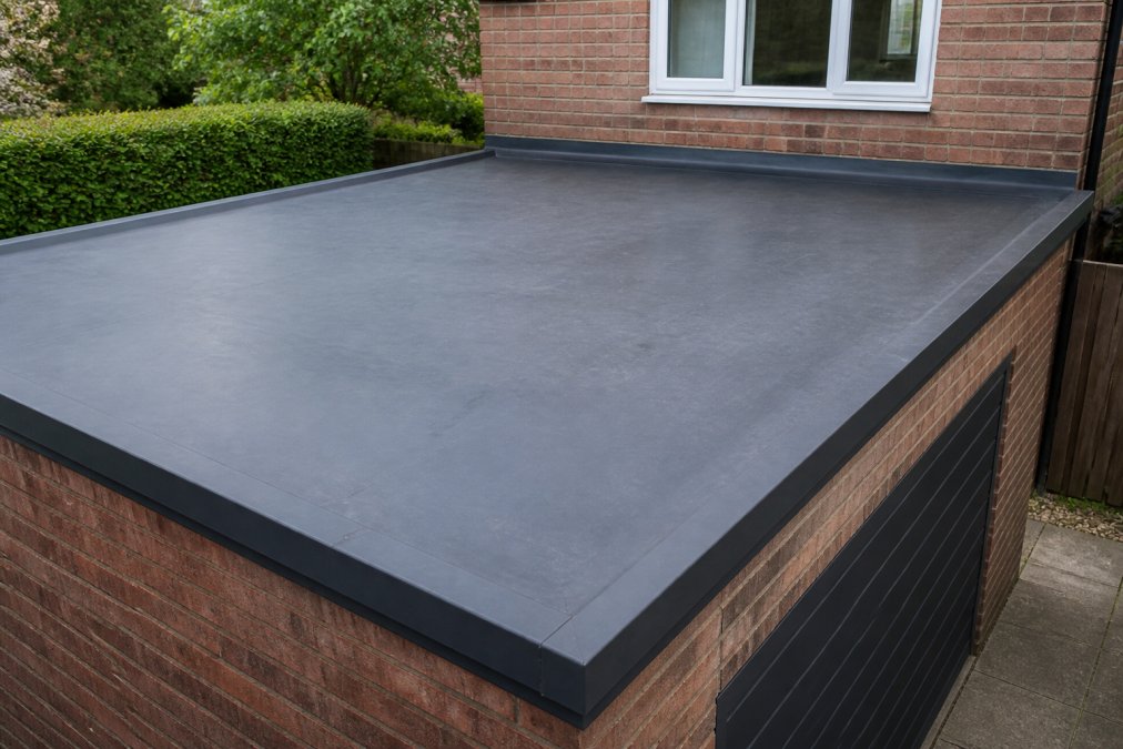 A close-up of a smooth, dark grey EPDM rubber membrane laid flat on a garage roof, with clean edges and neat flashing details visible around the perimeter, photographed in natural daylight