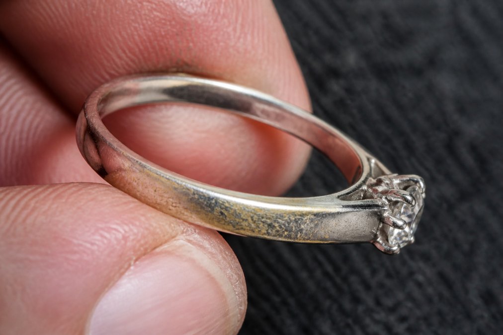 Close-up of white gold ring showing visible yellowing and wear on the band, with worn areas contrasting against less-worn sections under natural light