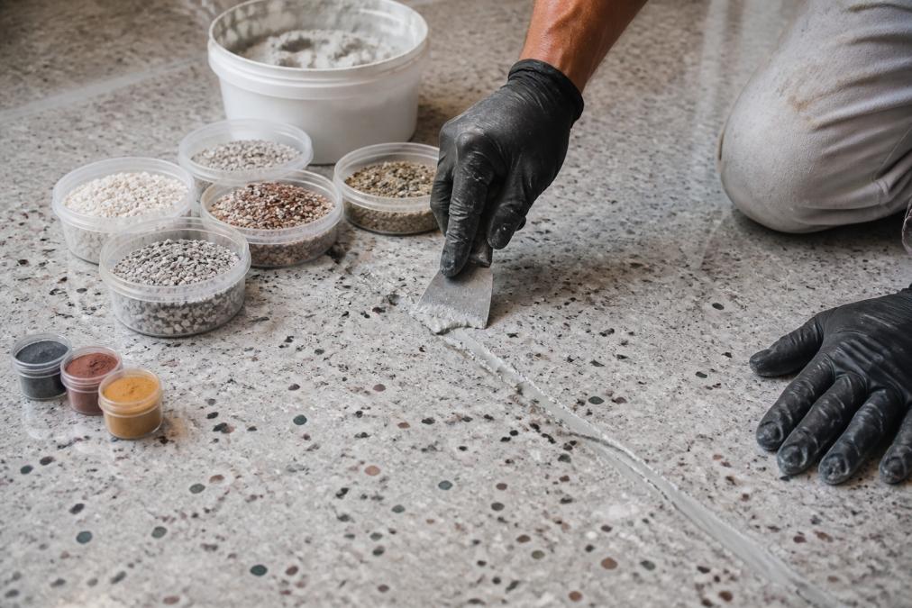 Technician using a putty knife to apply compound for terrazzo crack repair on a workshop table with color samples