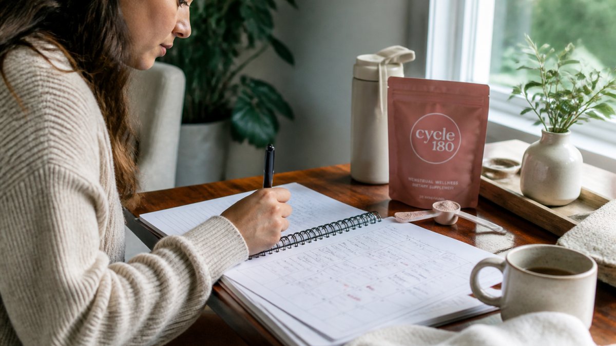 Woman writing in a detailed symptom journal with a pen, tracking daily notes about mood, energy, and cramping severity on a calendar page, natural window lighting