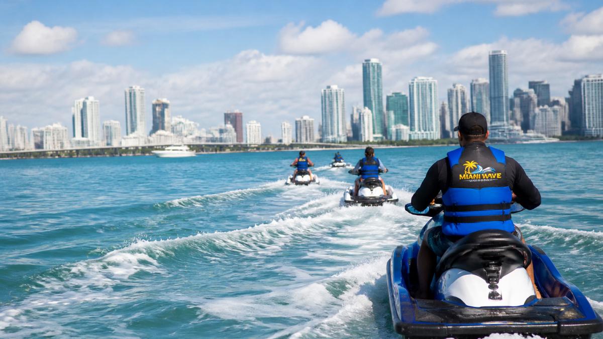 A guided jet ski tour cruising across Biscayne Bay with the Miami skyline in the background on a sunny day.