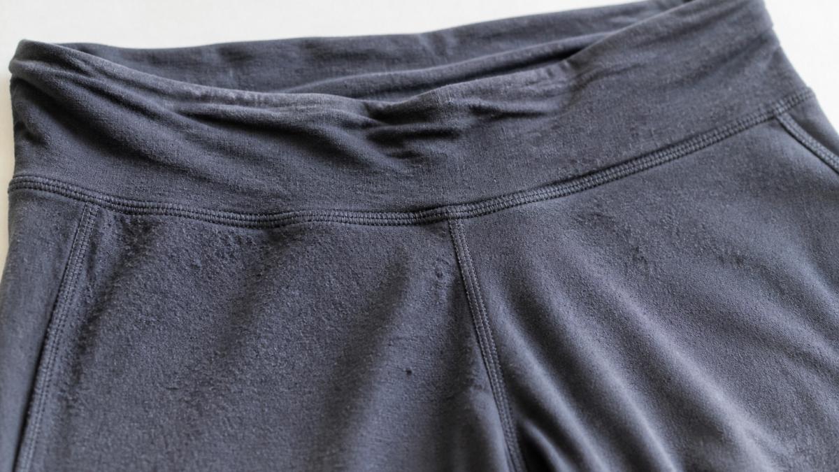 Close-up of worn athletic fabric showing pilling, stretched elastic waistband, and faded color on a pair of leggings laid flat on a light background