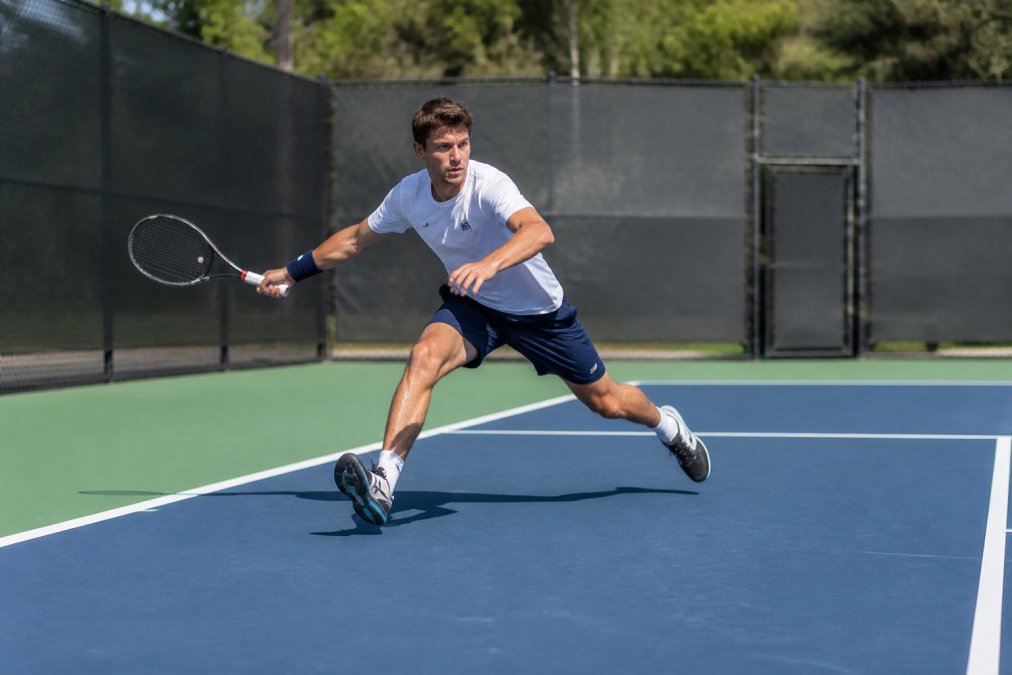 Competitive tennis player executing lateral movement drill on court, showing explosive acceleration from split-step position toward the sideline with proper weight transfer