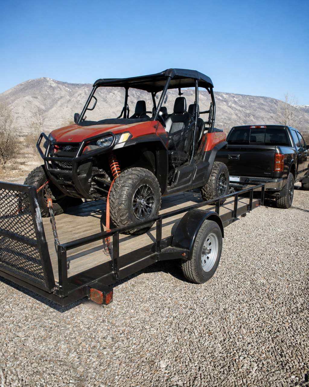 Side-by-side ATV loaded on an atv utility trailer parked behind a pickup truck on a gravel driveway
