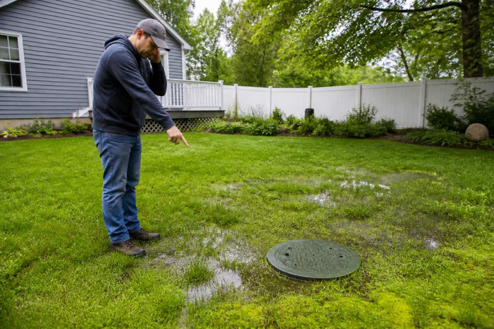 Homeowner looking at soggy grass and a septic tank lid, highlighting why you should know how often should septic tanks be