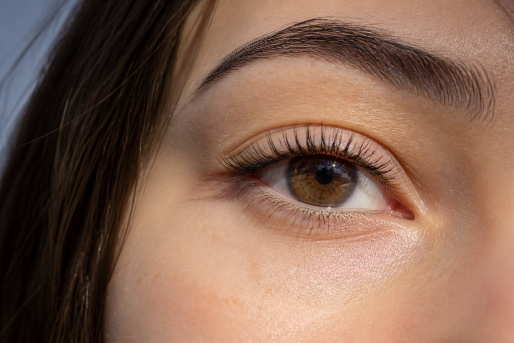 Close-up of a woman's eye with naturally lifted lashes in soft daylight, showing the upward curl without heavy makeup, skin glowing and unretouched