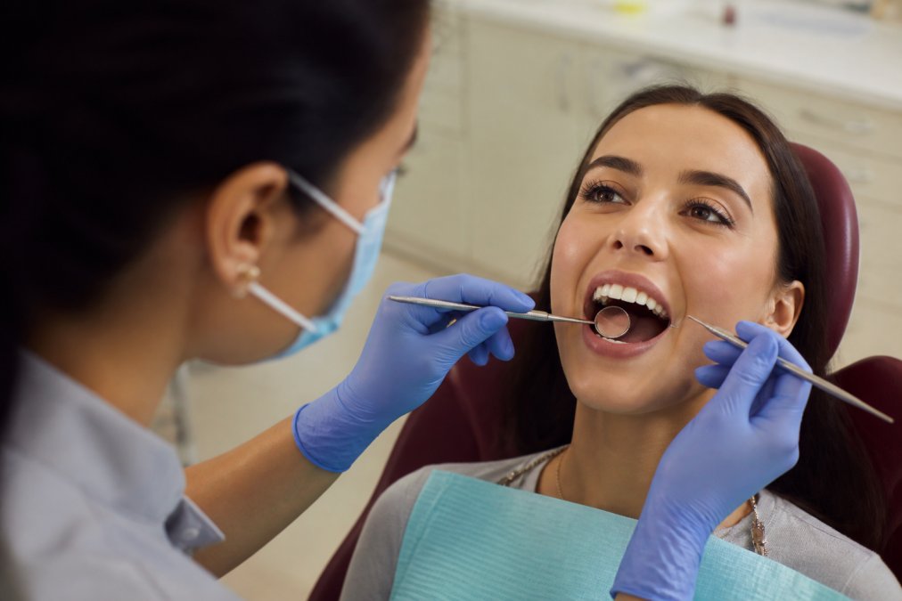 Close-up of dental professional examining patient's mouth with mirror and explorer tool during oral examination, bright clinical lighting