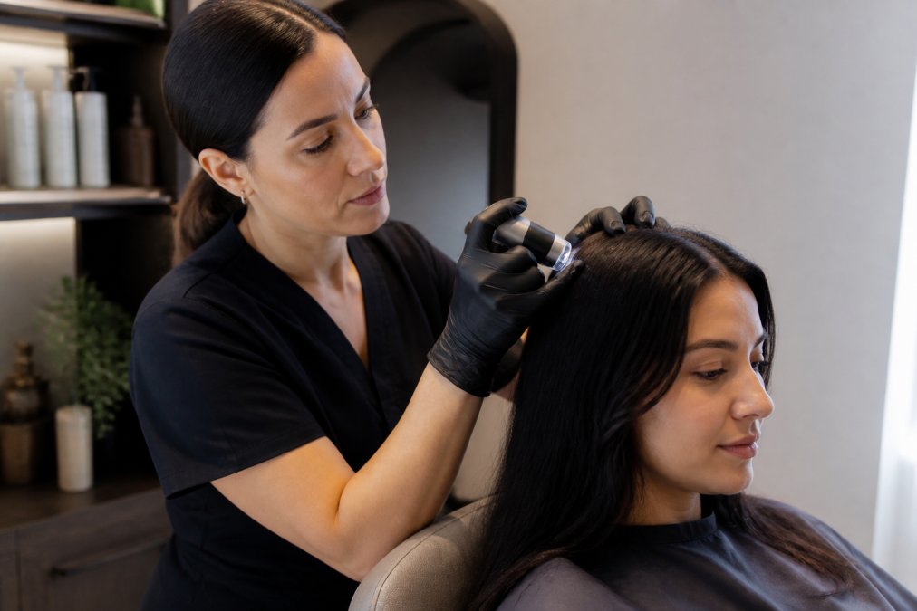 Professional trichologist examining a woman's scalp using a dermatoscope under clinical lighting in a modern wellness spa setting