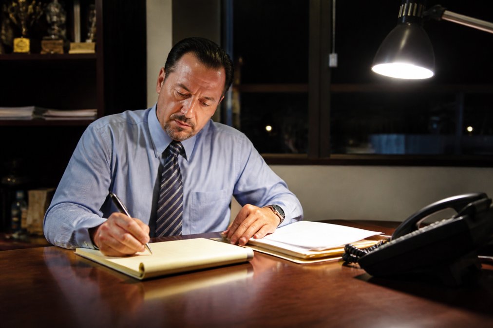 Professional bail bondsman in an office setting at night with desk lamp on, available to assist clients, working on paperwork with phone nearby