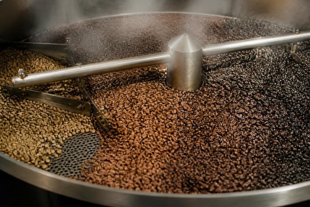 Close-up of freshly roasted coffee beans cooling in a roasting drum, steam rising, showing rich brown color and texture of beans at various roast levels from light to dark