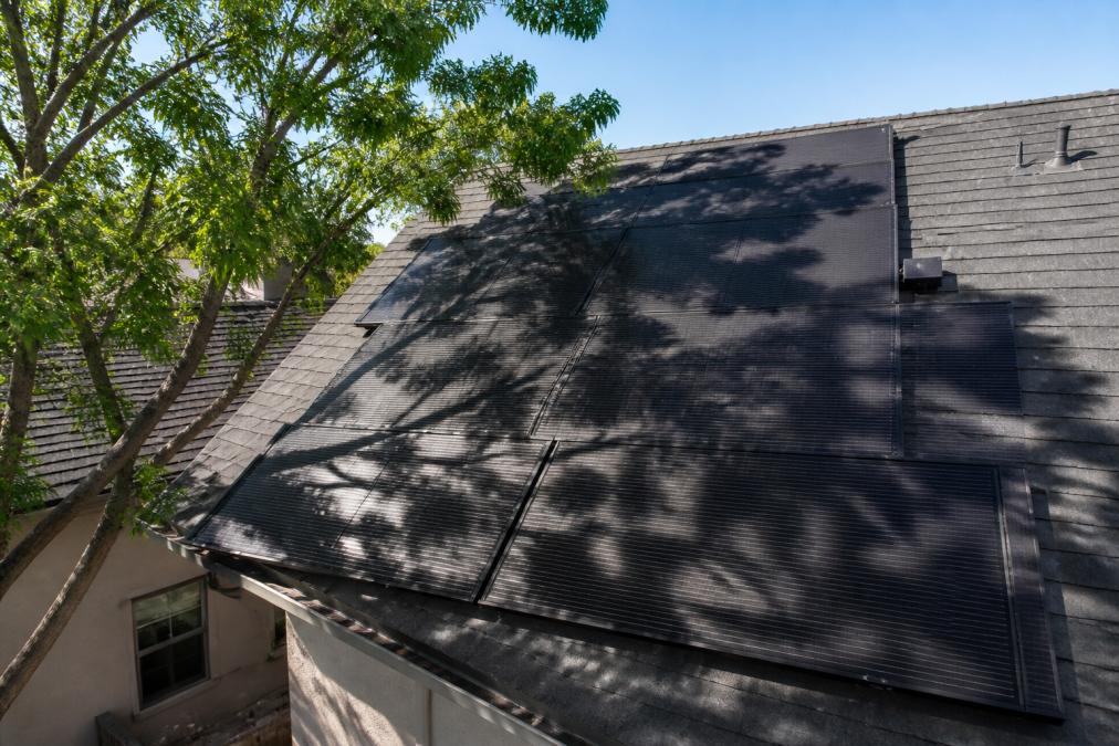 Solar pool heating panels installed on residential roof with tree shadows casting across panel array during afternoon hours, showing dappled shade patterns
