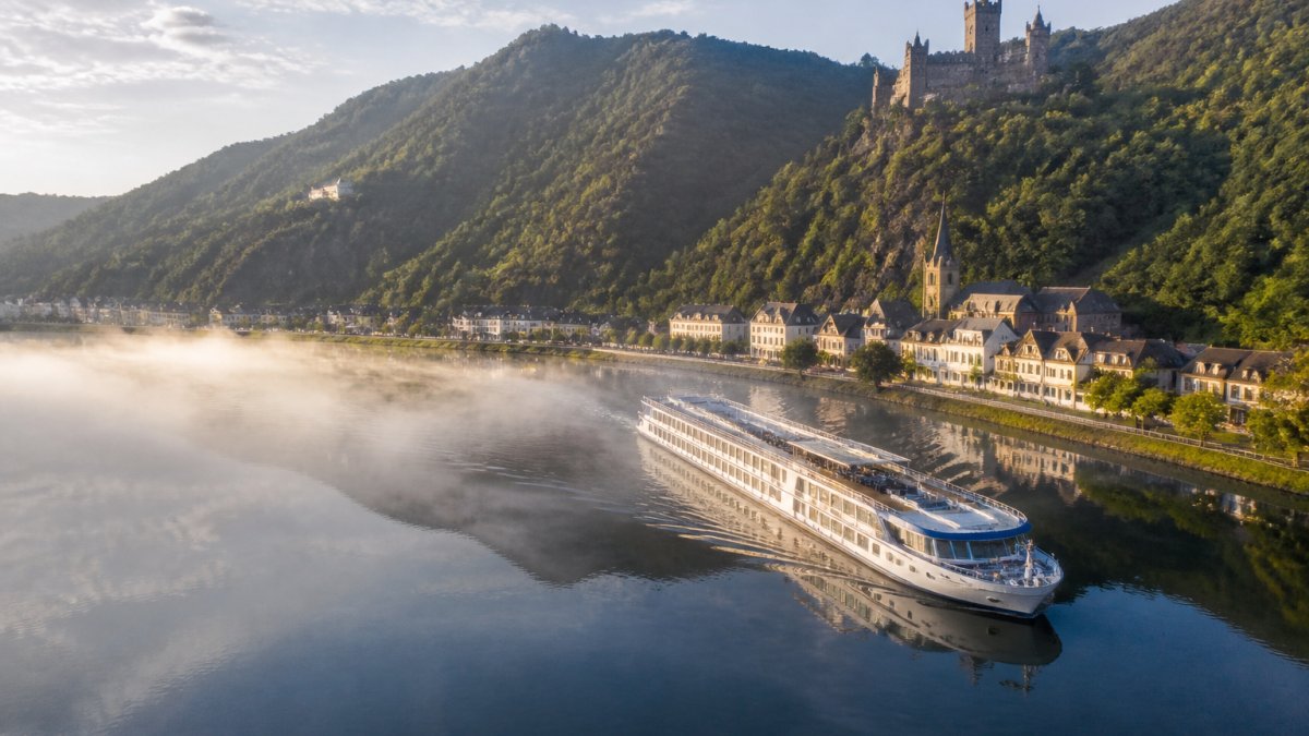 A river cruise ship sails through a misty European valley with historic castles for European river cruise planning.