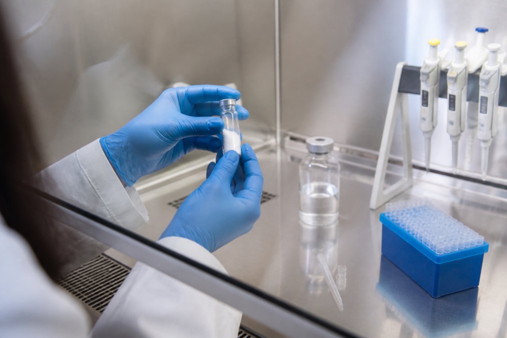 Researcher's hands carefully handling a lyophilized peptide vial with sterile reconstitution buffer and calibrated pipettes on a clean laboratory bench under bright task lighting