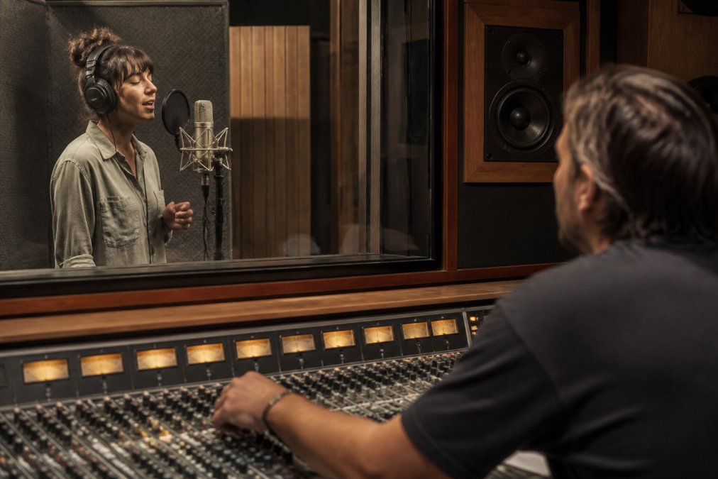 Vocalist recording in a studio booth with a pop filter to ensure vocal clarity as the engineer monitors levels