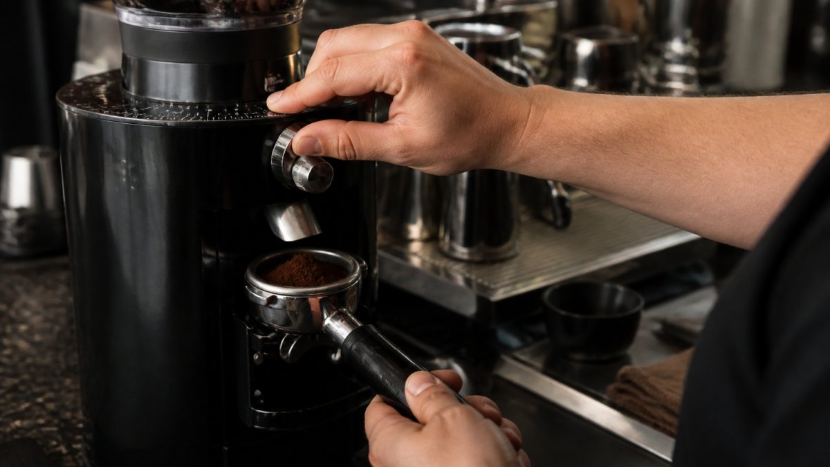Barista using a dial to adjust coffee grind size on an espresso machine with a portafilter nearby