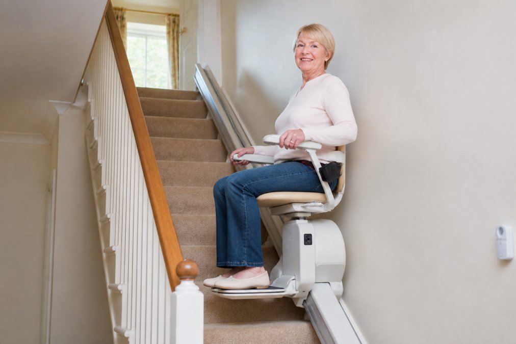 Person seated on an installed stairlift midway up a residential staircase, demonstrating safe positioning and the chair's secure mounting