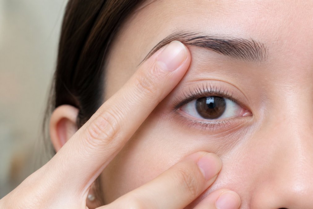 Close-up of a woman's clean, makeup-free eye with eyelid gently held taut, showing freshly curled natural lashes before any lash band is applied