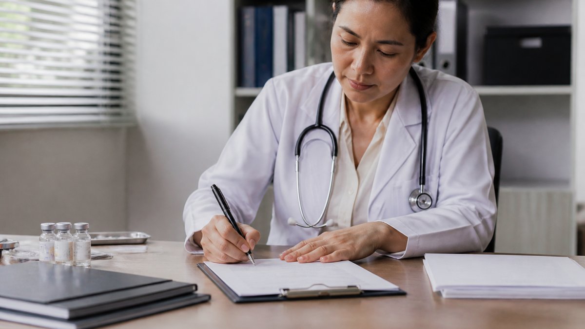 Doctor writing a detailed medical note at a desk with a stethoscope to support how to ask for workplace accommodations for