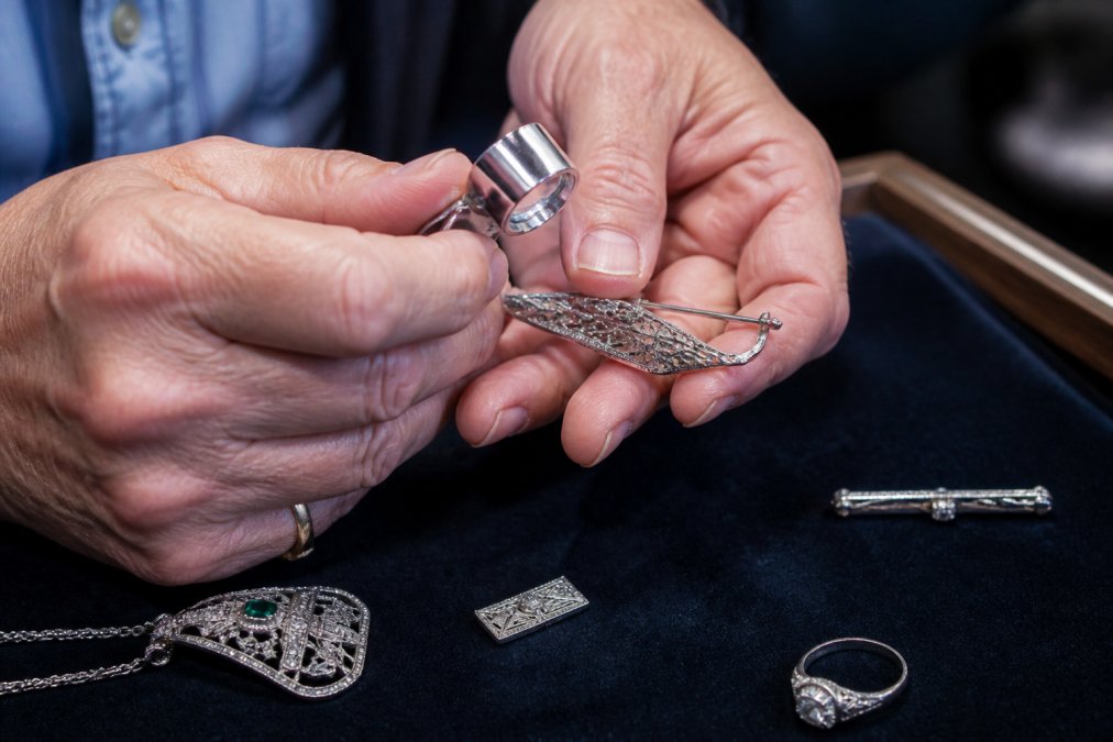 Jeweler using a loupe to inspect a hallmark on an Art Deco jewelry platinum brooch clasp