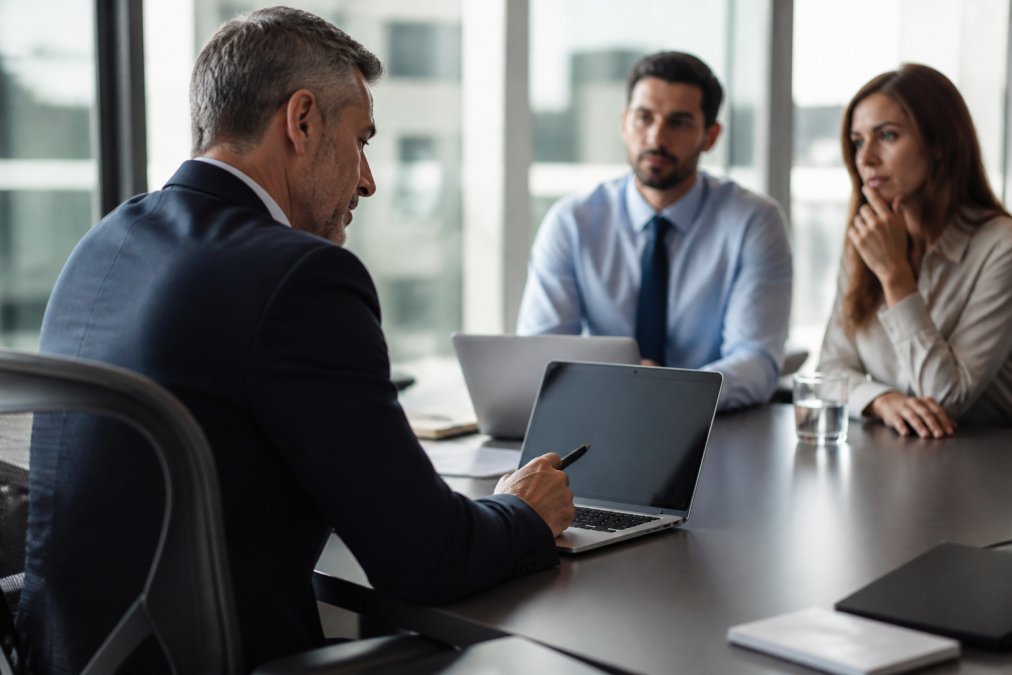 CISO or IT director reviewing security metrics and automation performance data on a laptop during a meeting with colleagues in a professional office setting