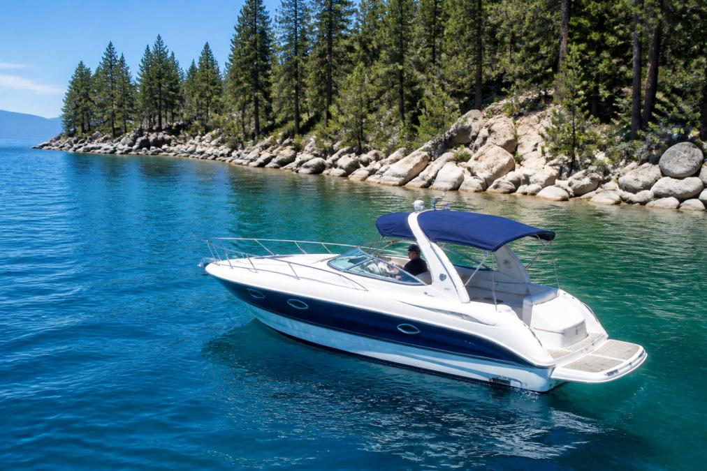 A private boat cruising on the clear blue water of Lake Tahoe near a quiet, forested shoreline, with no other boats visible in the frame