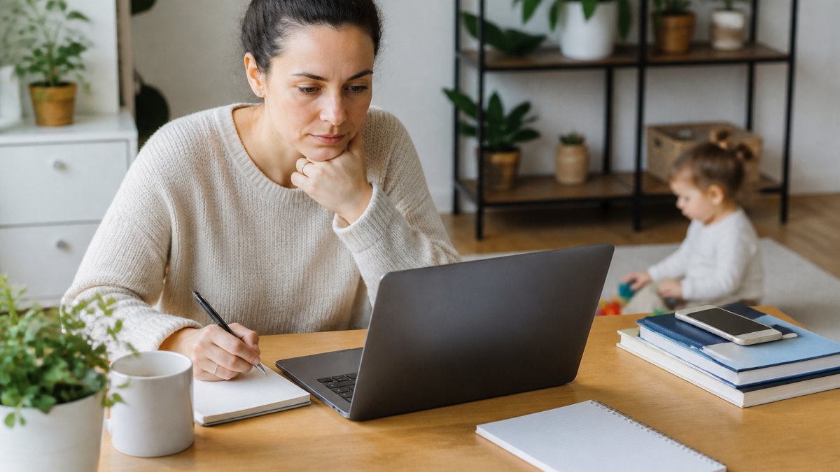 Parent working calmly on a laptop at a tidy desk to avoid technical headaches while a child plays nearby