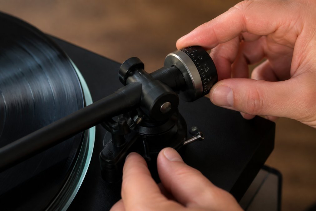 Close-up of hands carefully adjusting the counterweight on a vinyl turntable tonearm, showing the floating position with dial markings visible in natural studio lighting