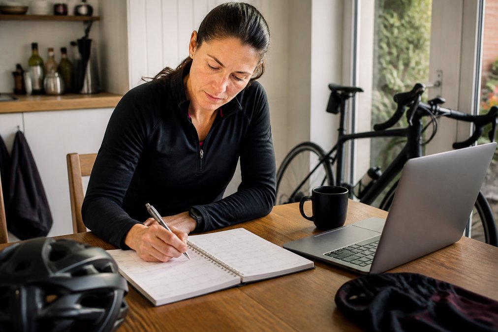 Infographic mapping a weekly triathlon training schedule at a kitchen table with a planner and laptop