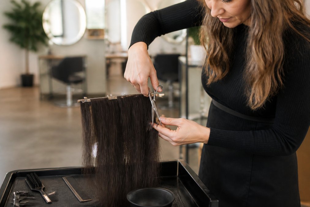 Professional hair stylist point cutting the ends of hair extensions with sharp scissors in a bright salon, focusing on the blending technique