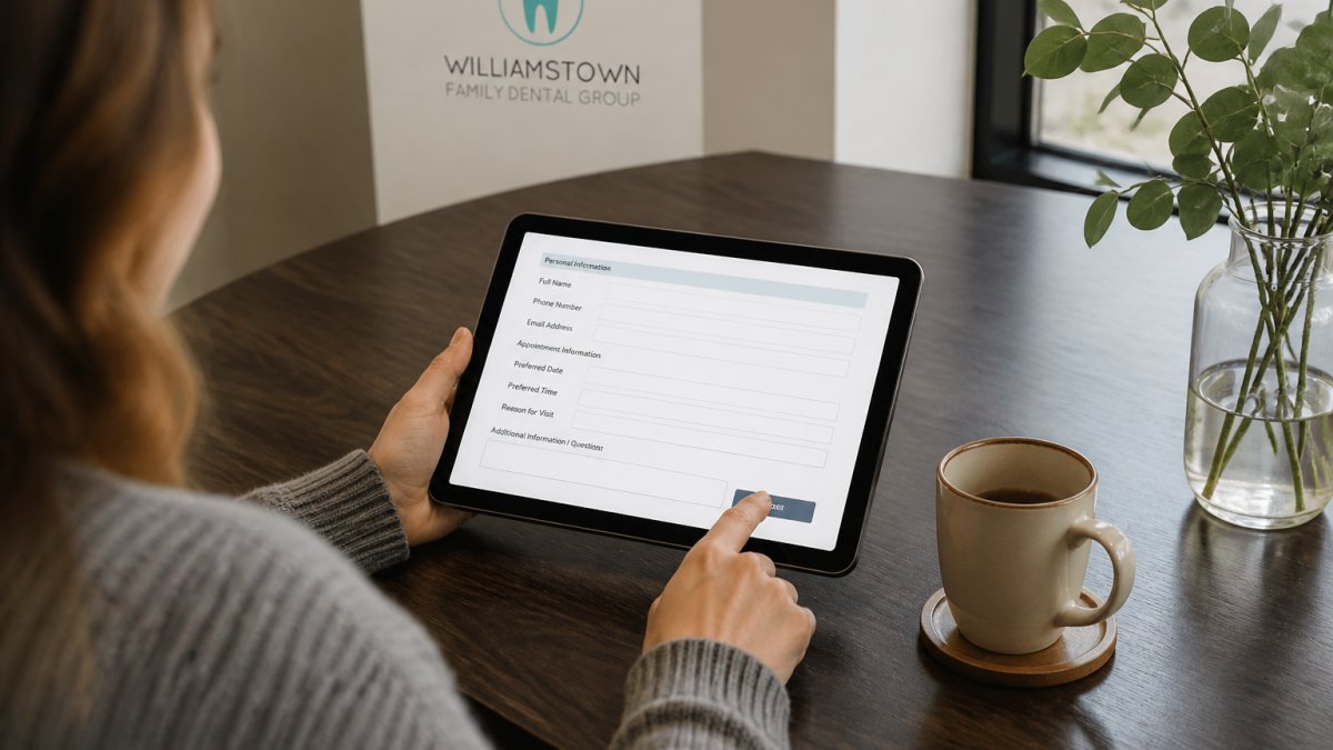 Person's hands using a tablet to complete an online dental appointment form while seated at a desk with a warm beverage nearby