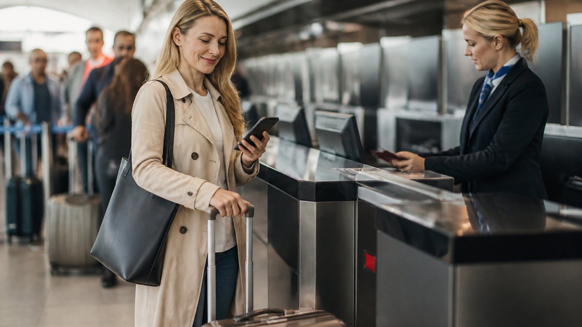 Passenger at airport check-in counter with luggage, looking at their phone with a satisfied expression, natural airport lighting
