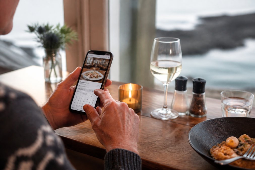 Close-up of hands using a smartphone or tablet to navigate a restaurant booking website, with a reservation confirmation visible on screen