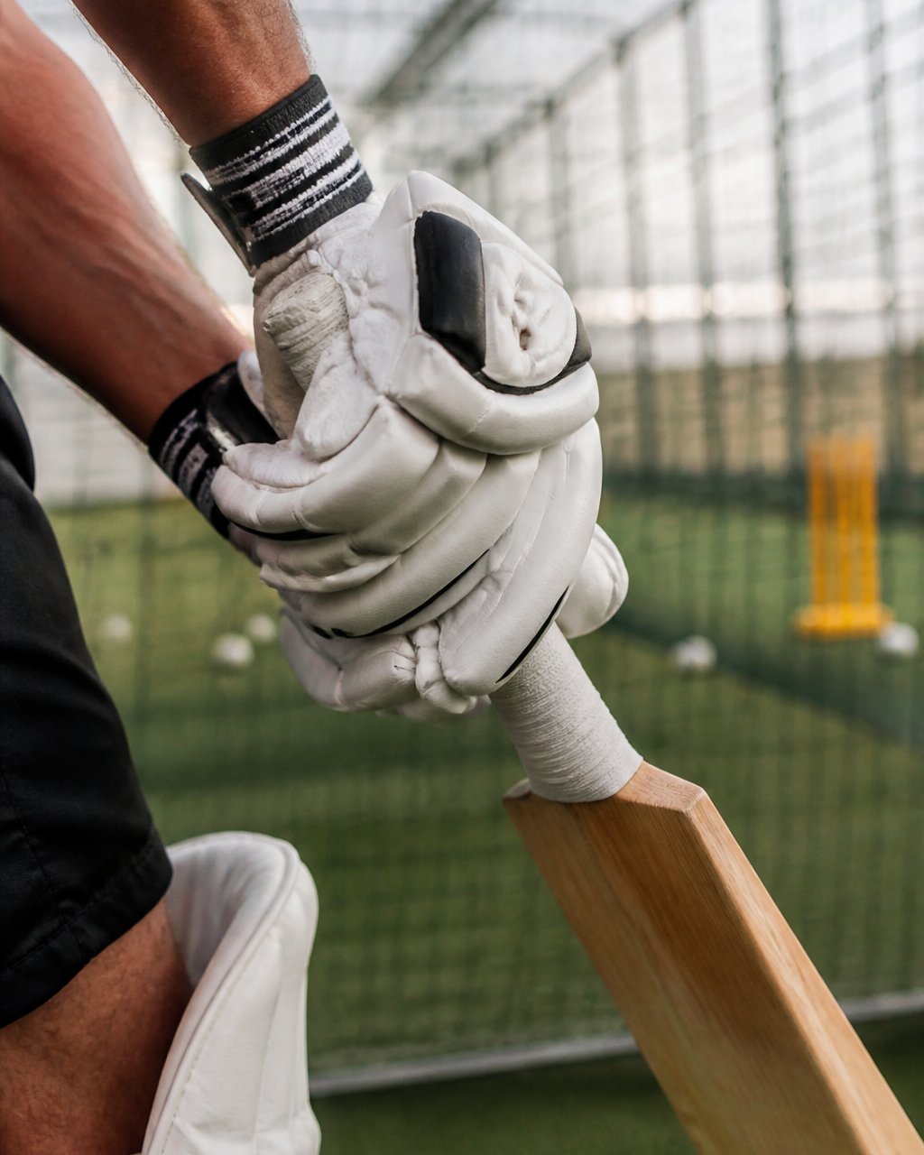 Close-up of a cricketer's gloved hands gripping a bat handle during a net session, showing the leather creasing naturally at the knuckles and palm