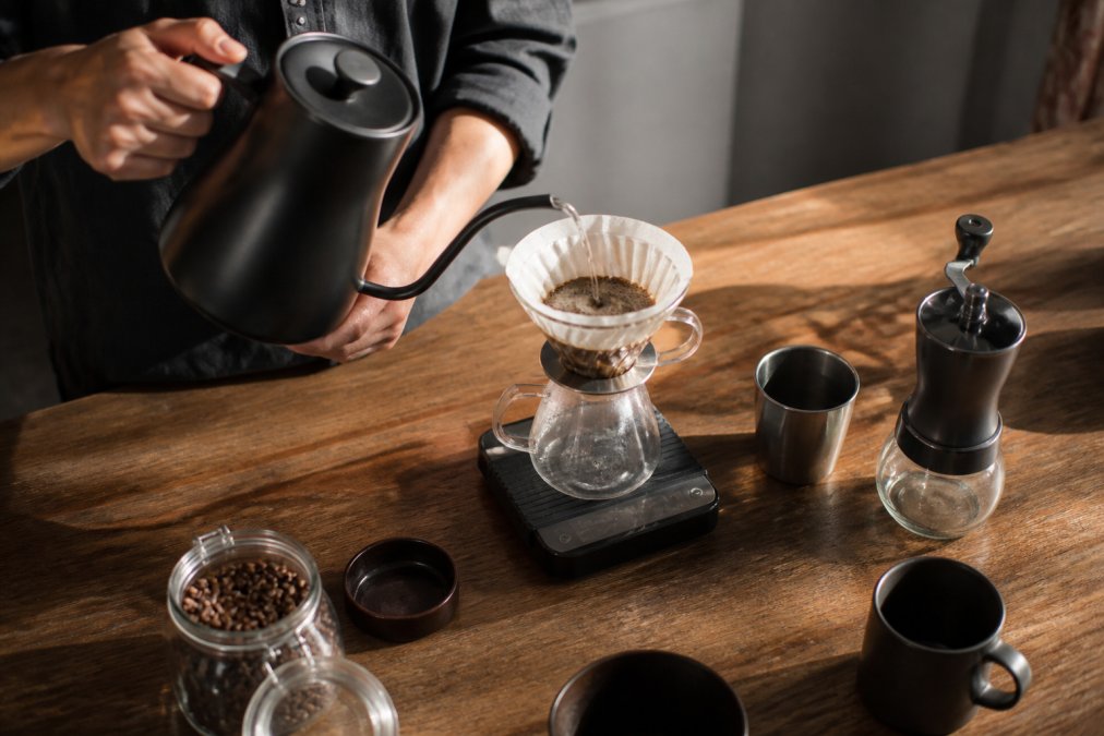 Hands pouring hot water from a kettle over coffee grounds to brew better coffee using a pour over dripper.