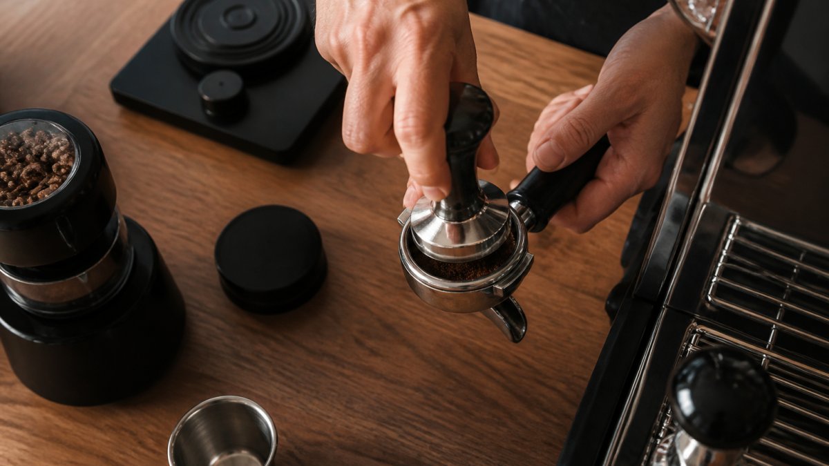 Barista using a metal tamper to press espresso grounds level into a portafilter basket
