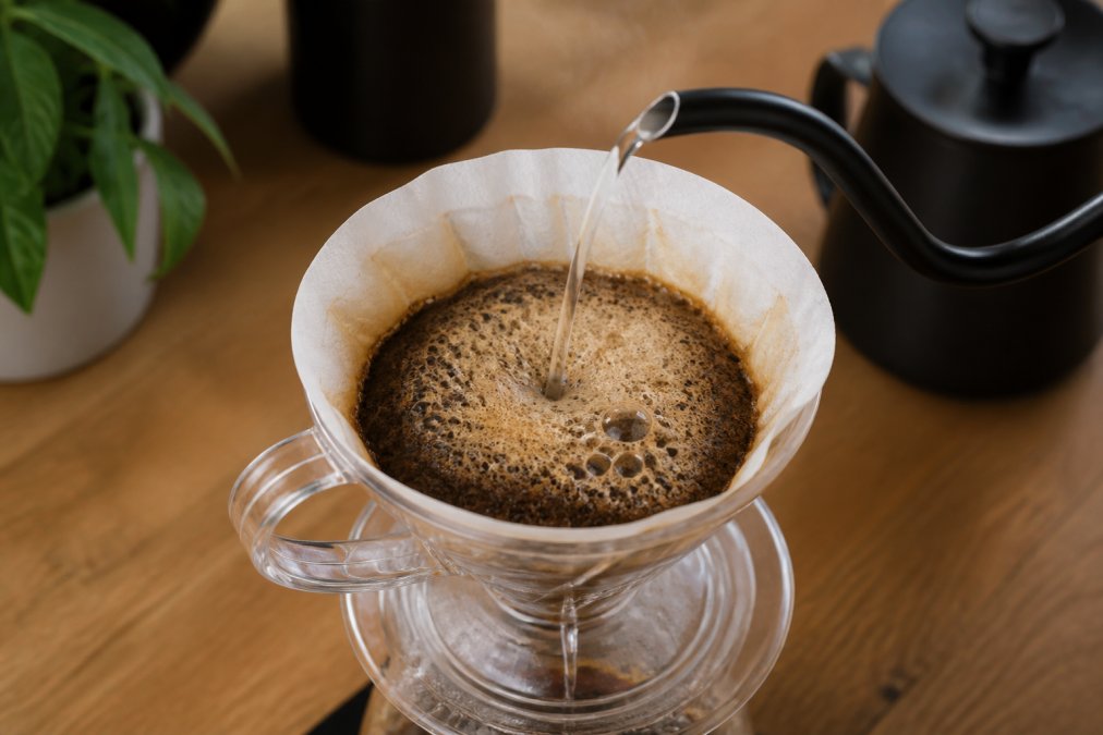 Hot water from a gooseneck kettle creates bubbles on coffee grounds to brew fresh coffee in a pour-over dripper.
