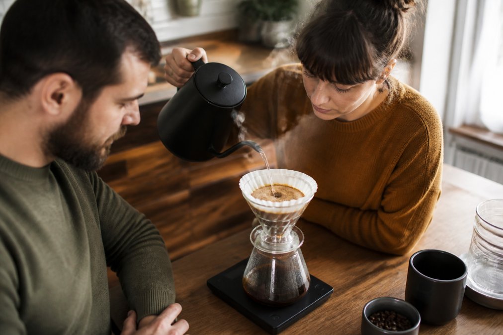 Gooseneck kettle pouring hot water over grounds to brew specialty coffee in a pour-over dripper on a digital scale