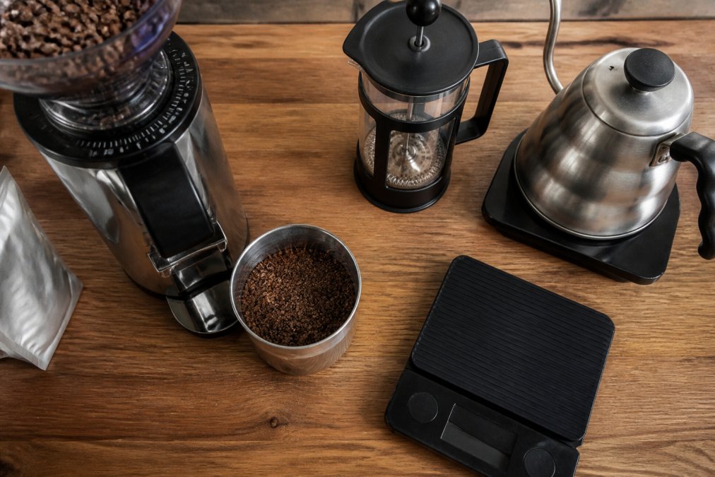 Coarse coffee grounds in a burr grinder beside a French press to brew specialty coffee on a kitchen counter