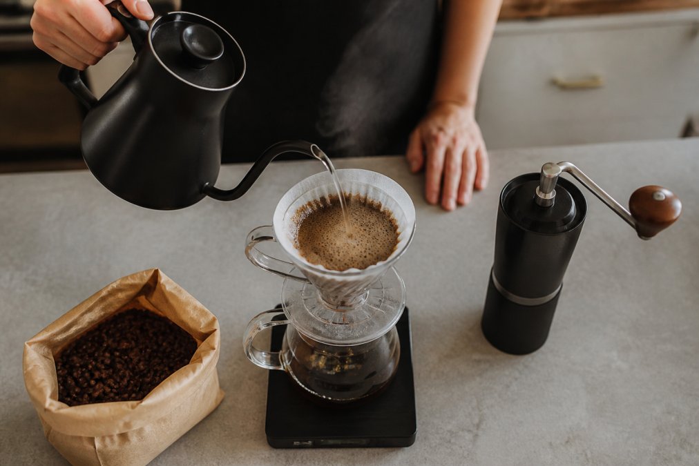 Hand pouring water from a gooseneck kettle to brew specialty coffee using a pour-over dripper and scale.