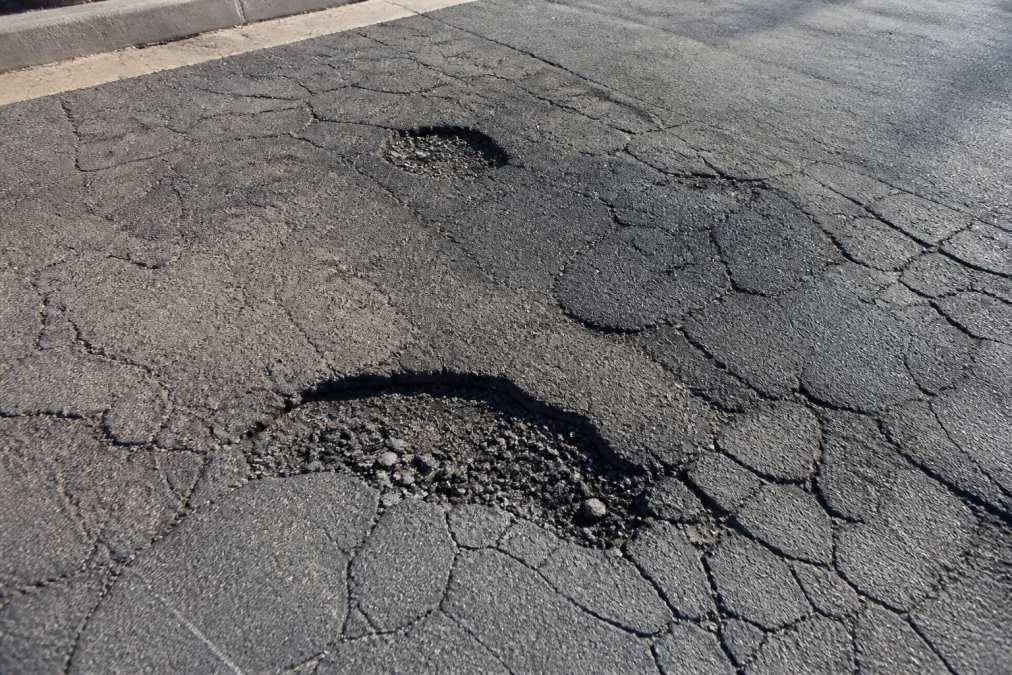 Infographic visualizing how to budget for commercial parking lot repairs by identifying asphalt cracks and potholes.