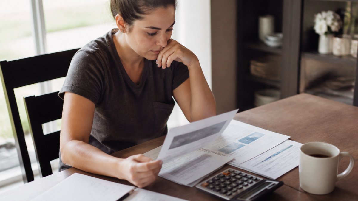 Person sitting at a table with a notepad and calculator, reviewing dental paperwork and treatment estimate documents while planning their budget, with natural window lighting