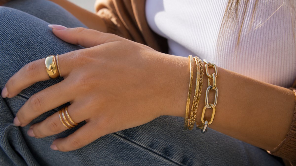 Close-up of a woman wearing a layered gold link bracelet and stacked rings on her wrist and fingers.