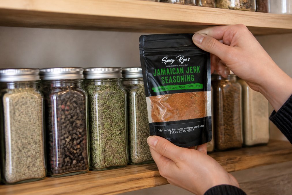 Close-up of hands arranging premium spice jars on a kitchen shelf, showing various seasonings including whole peppercorns and dried herbs with visible labels