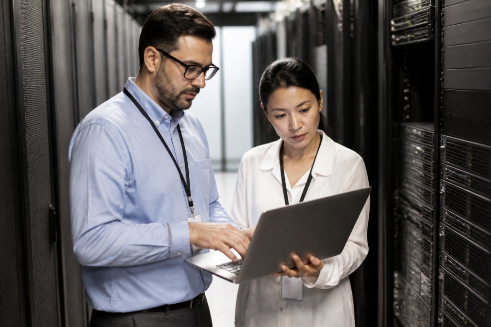 An IT manager and a developer reviewing server rack configurations on a laptop in a secure on-premises data center room