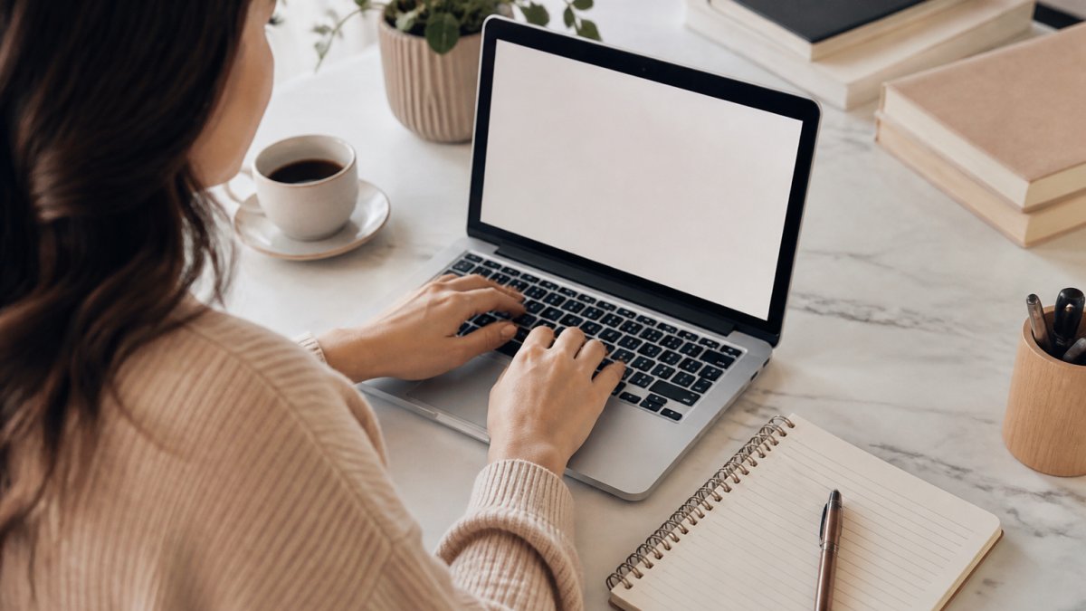 A marketing professional drafting a personalised email to an influencer on a laptop, with a notebook of creator names and a coffee cup on a bright desk