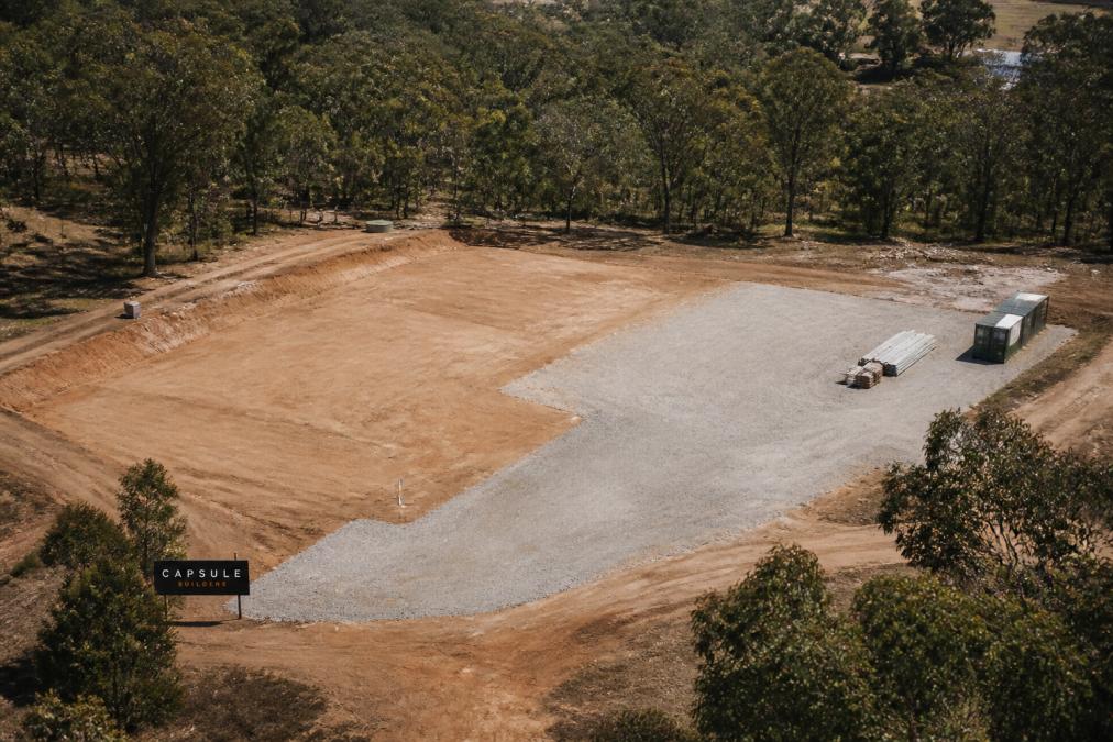Aerial view of a cleared regional property with marked utility connection points, levelled foundation area, and gravel staging zone prepared for modular home delivery and assembly